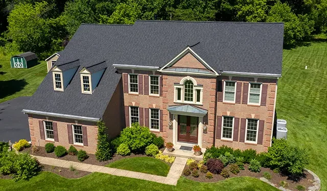 Aerial view of a two-story brick home with dormer windows, a centered front door, and a manicured lawn with shrubs.