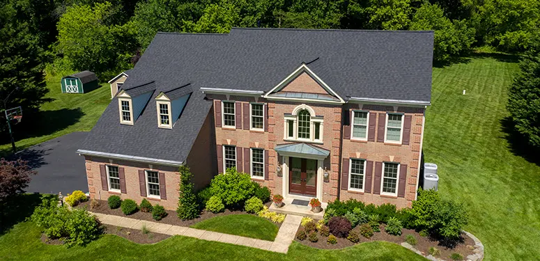 Aerial view of a two-story brick home with dormer windows, a centered front door, and a manicured lawn with shrubs.