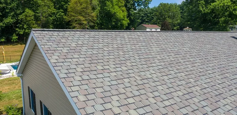Aerial view of a sloped residential roof covered with gray-brown asphalt shingles, with green trees in the background.