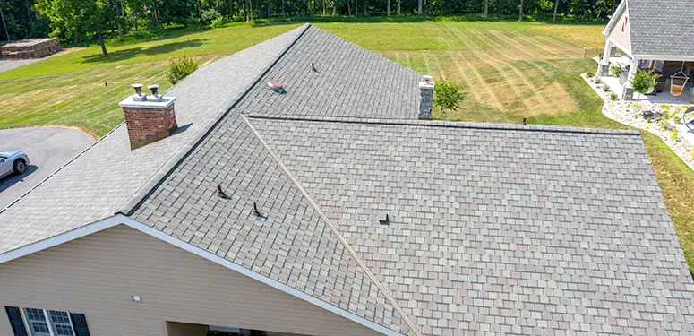 Aerial view of a suburban house roof with gray shingles, multiple slopes, two chimneys, and vents.