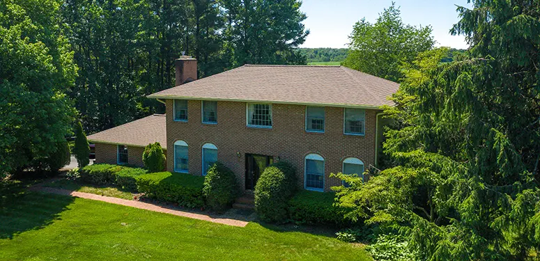 Brick two-story house with arched windows, front garden hedges, and surrounding trees in a lush yard.