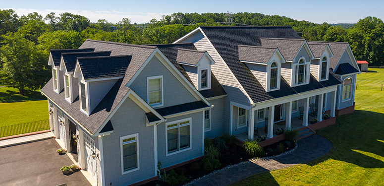 Two-story suburban house with multiple gabled roofs, light blue siding, front porch, and surrounding green lawn.