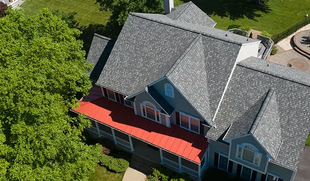Aerial view of a blue two-story house with a red front porch awning, surrounded by green trees and a playground in the background.