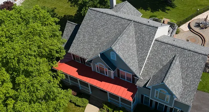 Aerial view of a blue two-story house with a red front porch awning, surrounded by green trees and a playground in the background.