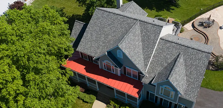 Aerial view of a blue two-story house with a red front porch awning, surrounded by green trees and a playground in the background.